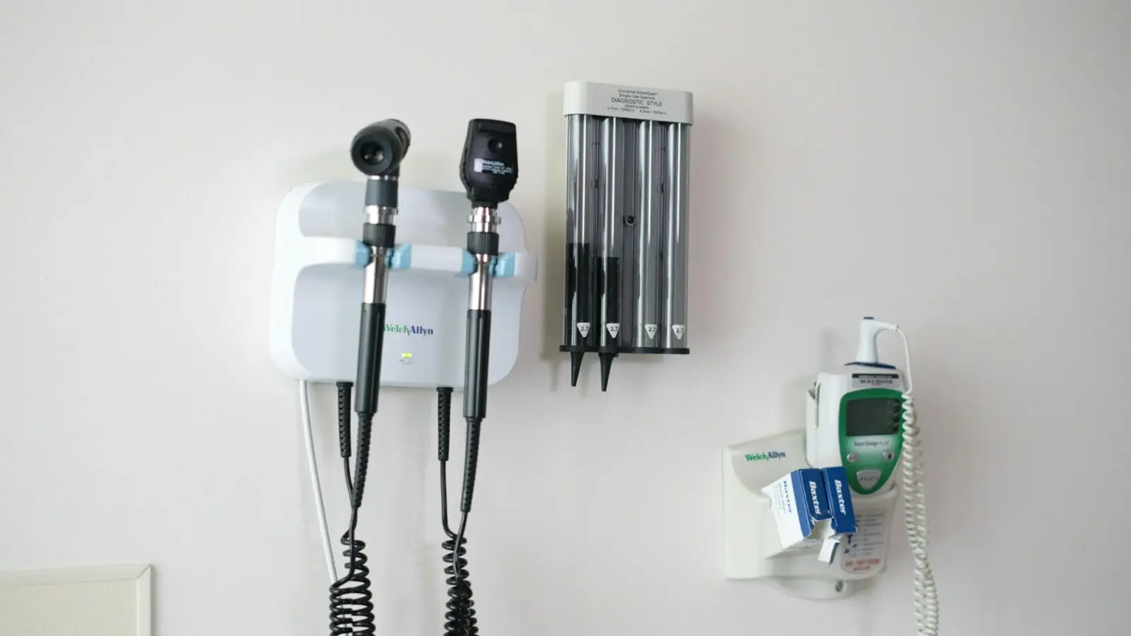 Instrumentos de exame médico presos à parede de um consultório: otoscópio, oftalmoscópio e termômetro