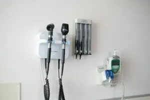 Instrumentos de exame médico presos à parede de um consultório: otoscópio, oftalmoscópio e termômetro