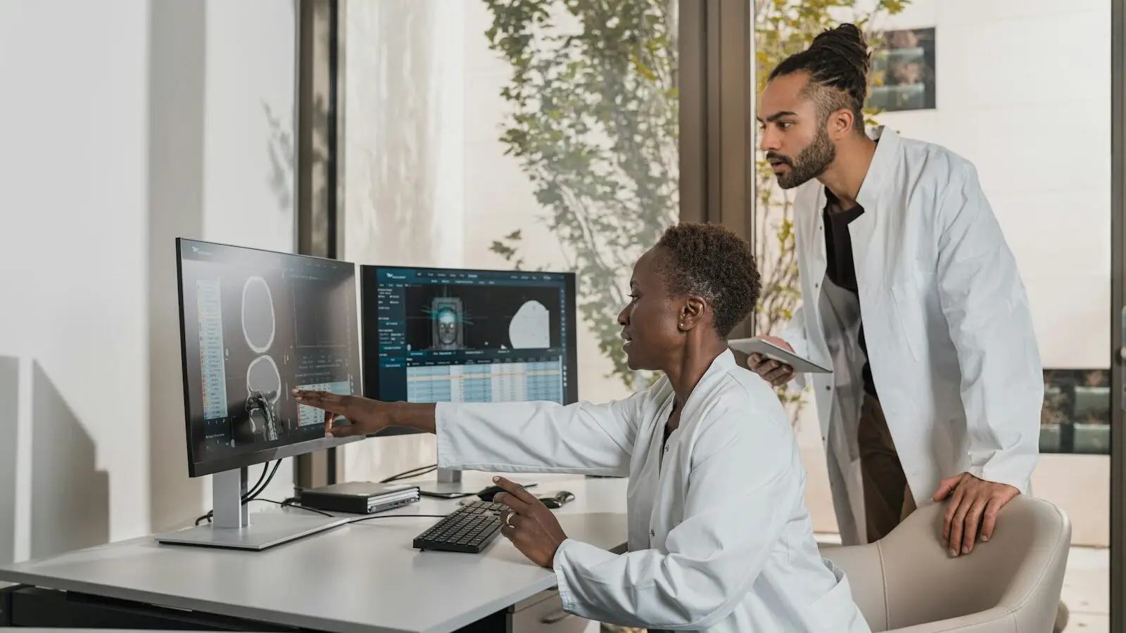 Dois profissionais de jaleco branco analisam um exame de imagem em monitores de uma clínica de diagnóstico