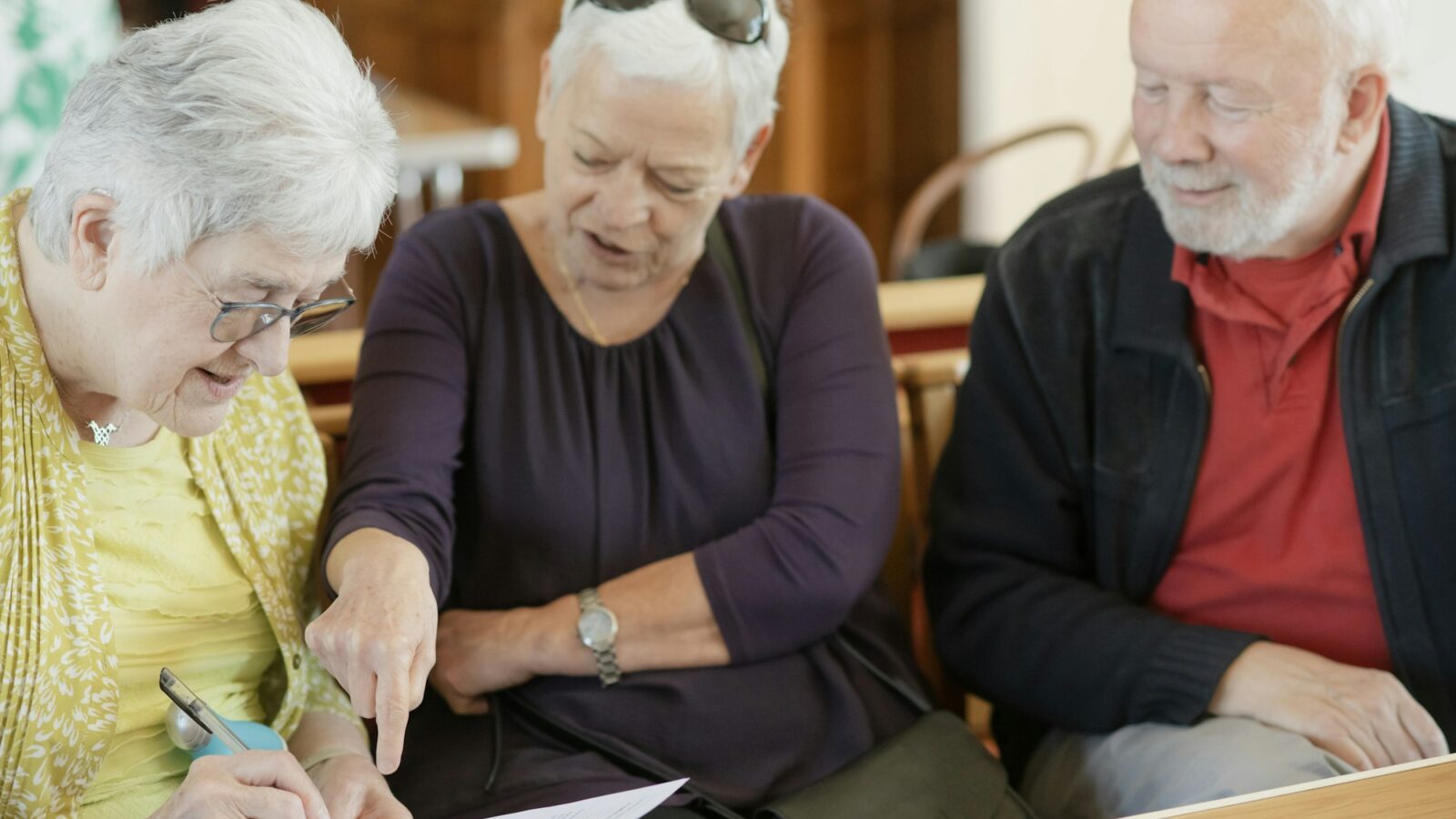 Três pessoas idosas sentadas a uma mesa conferem juntas um formulário de papel