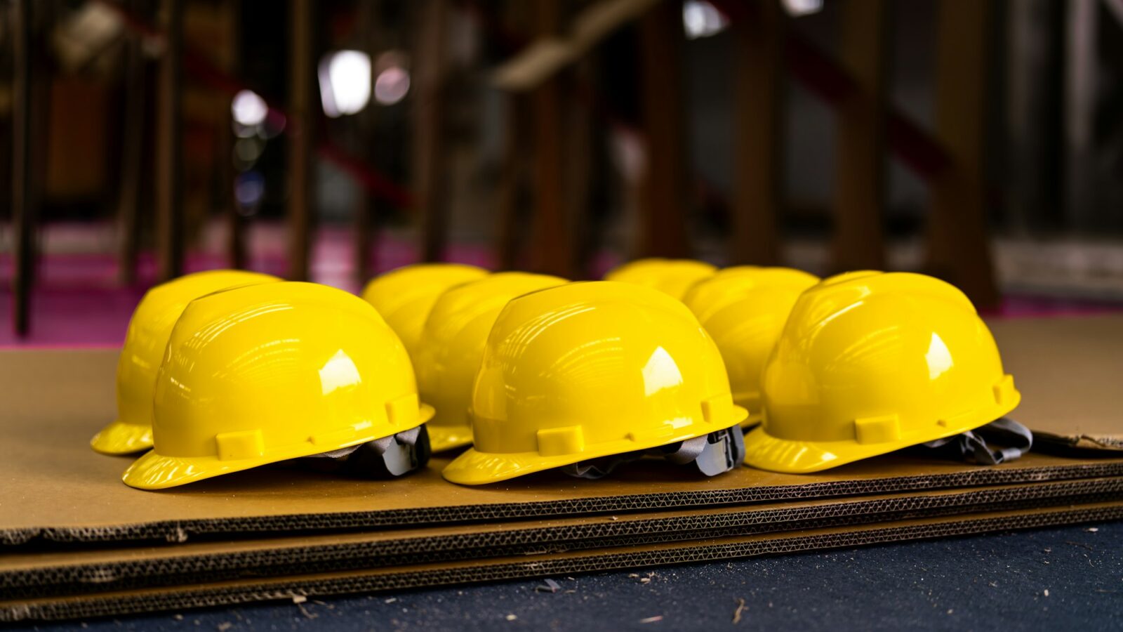 Capacetes de segurança amarelos enfileirados sobre placas de papelão em um canteiro de obras